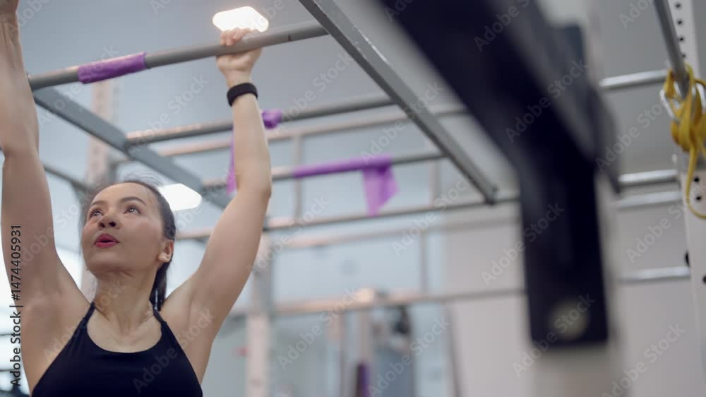 A woman is hanging from a bar. She is wearing a black tank top. The bar is purple A woman is hanging from a bar. She is wearing a black tank top. The bar is purple