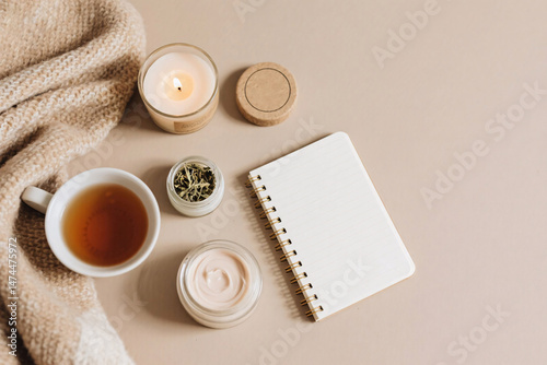 Flat lay scene with cozy diary, herbal tea cup, burning candle, organic balm in eco-friendly jar, and soft blanket, top view with emotional skincare feeling and empty area for text