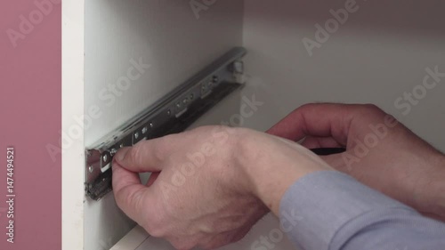 installing guides in furniture with a screwdriver, carpenter tightens screw into metal guides for drawer, furniture assembly