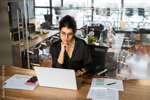 30s latin hispanic business woman working on laptop computer in modern office. Young indian or middle eastern businesswoman professional employee using pc doing online banking analysing. Copy space