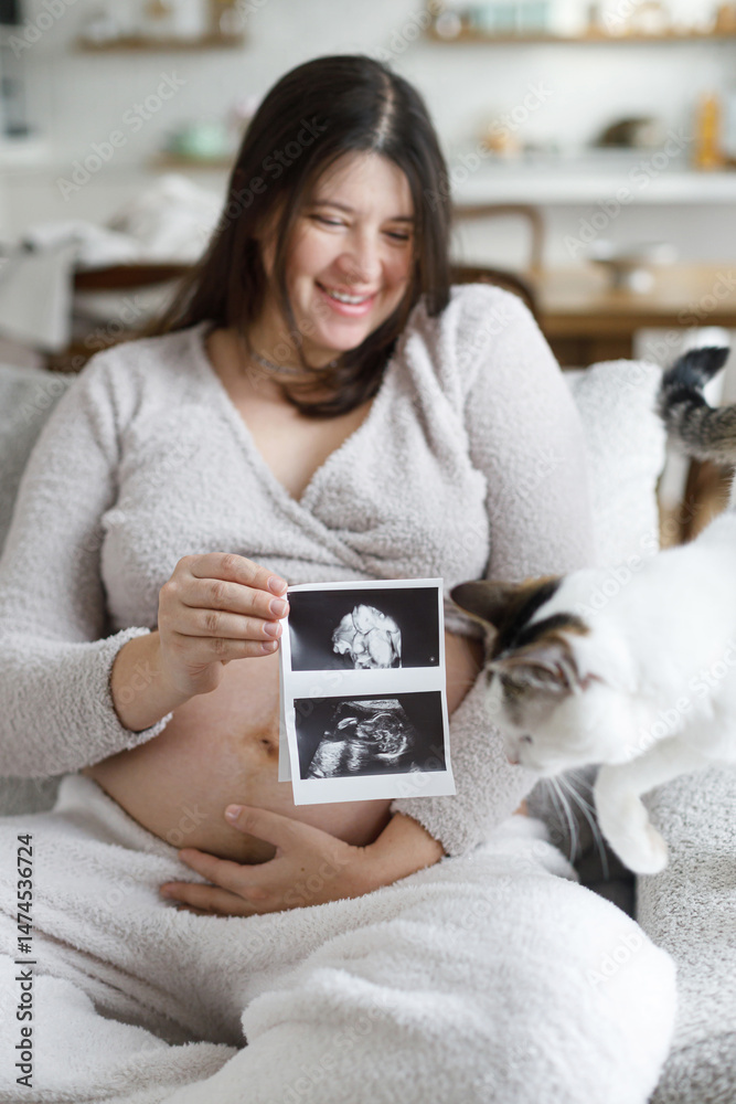 Pregnant woman hugging baby bump, holding ultrasound picture and relaxing on couch with cute cat in modern living room. Fertility and maternity. Happy Mothers day. Love and care concept Pregnant woman hugging baby bump, holding ultrasound picture and relaxing on couch with cute cat in modern living room. Fertility and maternity. Happy Mothers day. Love and care concept