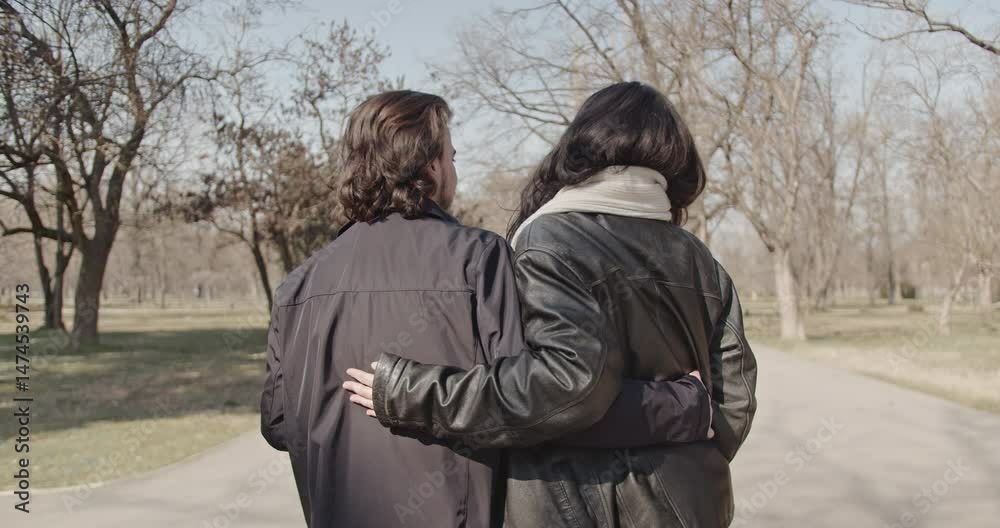 A happy couple in love walks together in a park on a sunny winter day. They enjoy each other's company as they stroll along the paved path. A happy couple in love walks together in a park on a sunny winter day. They enjoy each other's company as they stroll along the paved path.