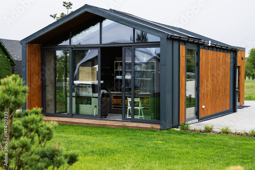 Modern tiny house with glass facade and wooden exterior in a green environment