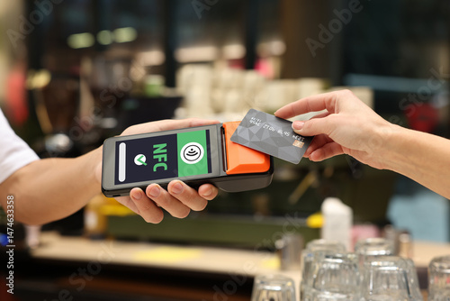 Payment terminal with NFC system. Client using credit card to pay for service in cafe, closeup