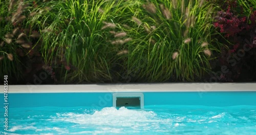 Backyard swimming pool with counter current system in operation, water actively circulating in front of garden plants
