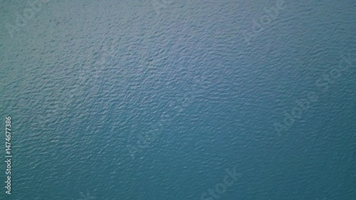 Aerial close-up view of sunlit sea surface with gentle ripples and deep green-blue tones. Natural ocean water texture with sunlight reflection and subtle wave patterns