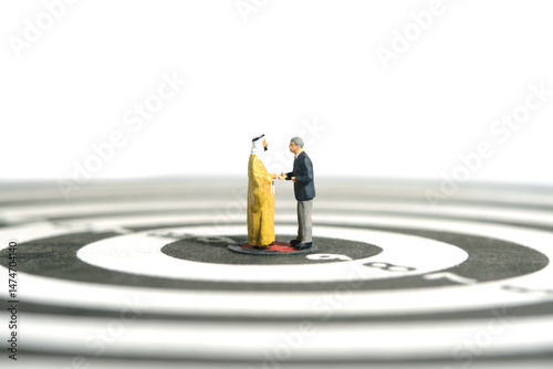 Miniature people toy figure photography. Partnership concept. A Sultan and businessman make an handshake agreement at the center of dartboard. Isolated on white background