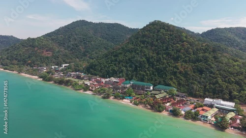 Turquoise waters gently lap against the sandy shores of koh chang island, thailand, where vibrant resorts nestle amidst lush green mountains, creating a picturesque tropical paradise