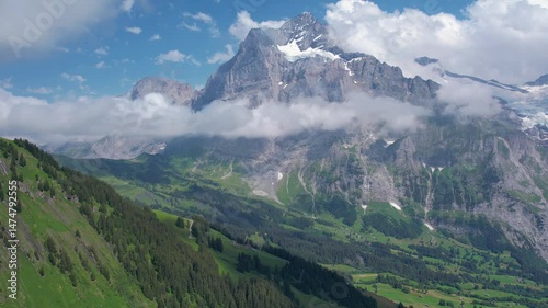 Cinematic drone fly over breathtaking view of Grindelwald surrounded by towering mountain peaks and lush green valleys. Snow-capped summits and scattered cloud. Travel and healthy lifestyle