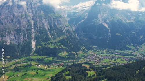 Cinematic drone fly over breathtaking view of Grindelwald surrounded by towering mountain peaks and lush green valleys. Snow-capped summits and scattered cloud. Travel and healthy lifestyle