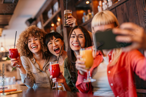 Canvas Print Cheerful friends taking selfie while drinking cocktails at the bar
