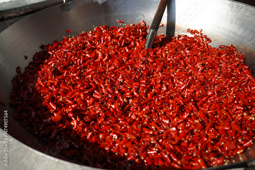 Fototapeta Naklejka Na Ścianę i Meble -  A large metal pan filled with bright red chopped dried chili peppers, suggesting preparation for cooking or spice production.