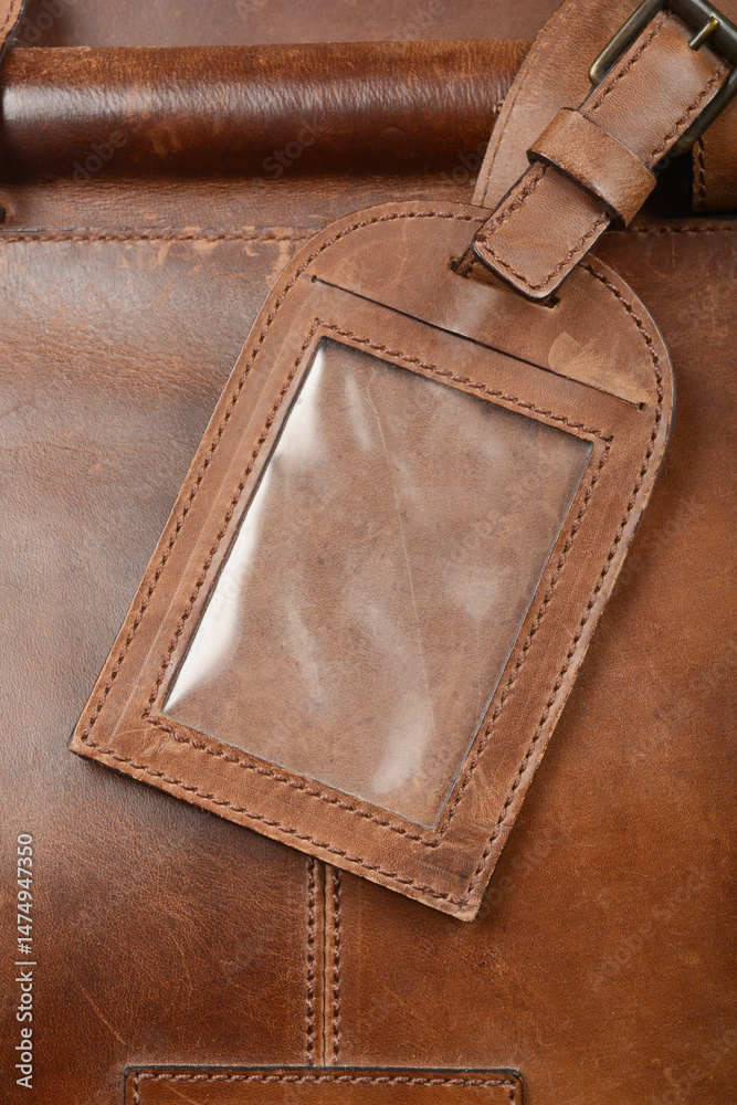 A close-up shows a brown leather luggage tag with a clear plastic window attached to a brown leather bag