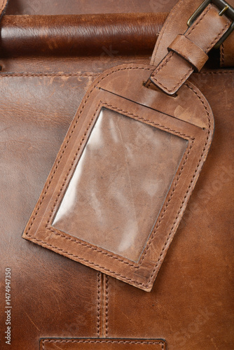 Obraz na płótnie A close-up shows a brown leather luggage tag with a clear plastic window attached to a brown leather bag w salonie