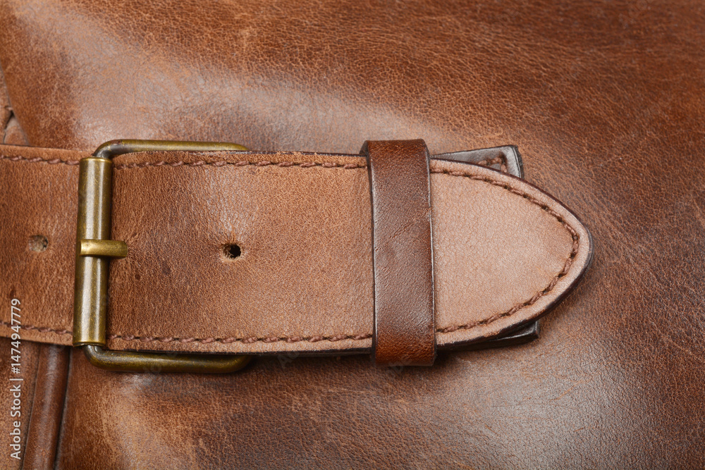 A close-up shows a brown leather strap with a brass buckle detail on a textured brown leather surface