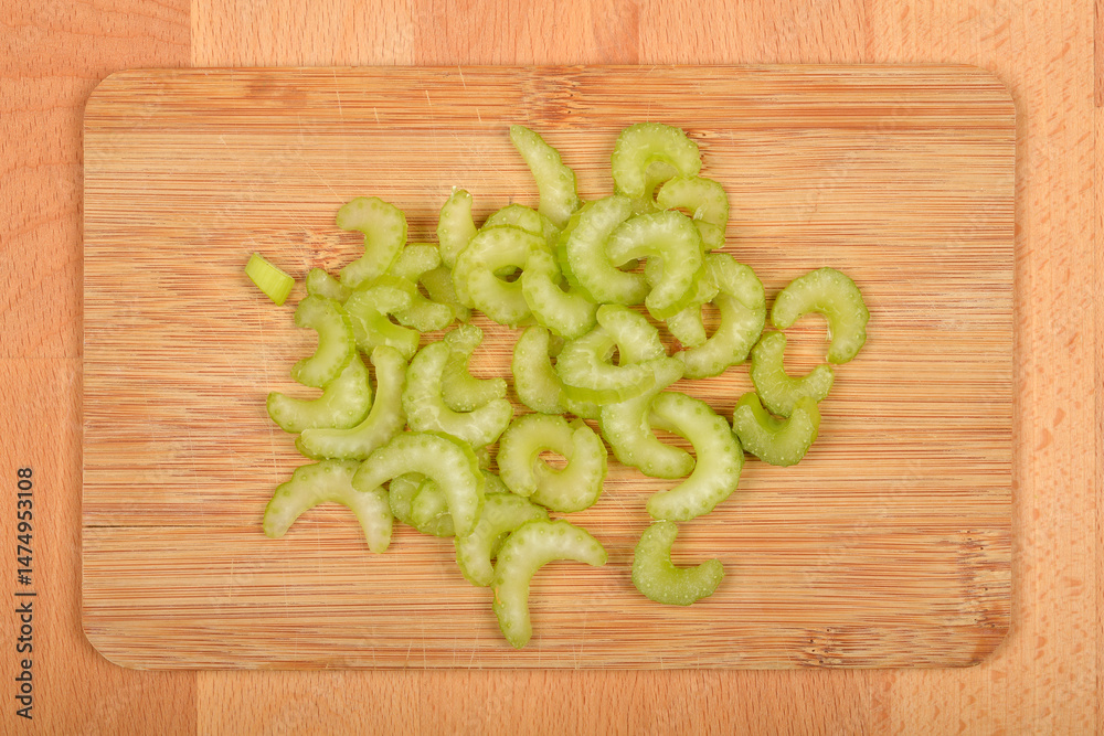 A top-down close-up shows sliced light green celery pieces scattered on a light brown wooden cutting board