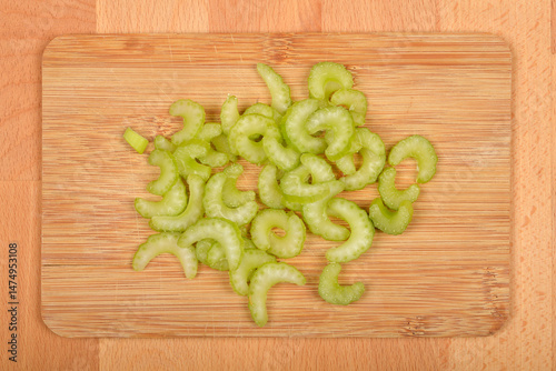 Obraz na płótnie A top-down close-up shows sliced light green celery pieces scattered on a light brown wooden cutting board w salonie