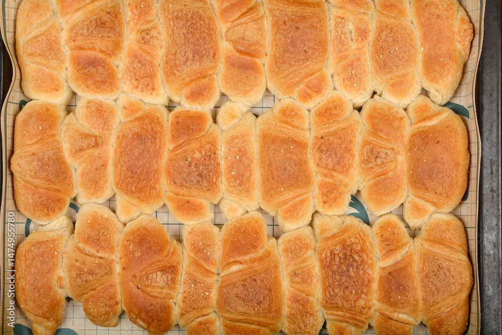 A top-down view shows rows of golden-brown baked mini croissants sprinkled with sesame seeds on a grid baking mat