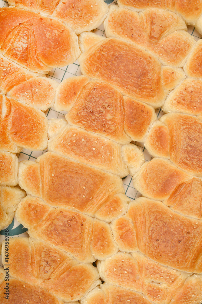 A top-down view shows rows of golden-brown baked mini croissants sprinkled with sesame seeds on a grid baking mat
