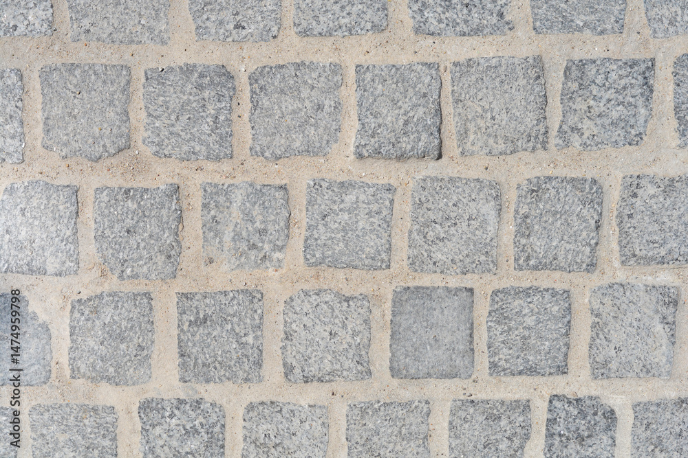 A close-up overhead view shows a section of a cobblestone pavement with square, gray stones and light-colored grout