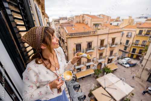 Fotografie A young woman enjoys coffee and a Sicilian cannolo on a balcony overlooking narrow Palermo streets