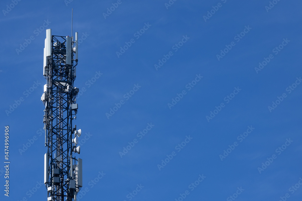 A tall communications tower equipped with antennas and satellite dishes stands sharply against a vivid blue sky, symbolizing modern technology and connectivity. Includes copy space.