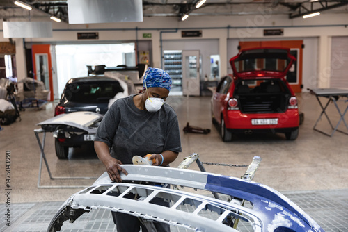 Detached car bumper getting sanded on metal stand in auto body shop with open hatchback