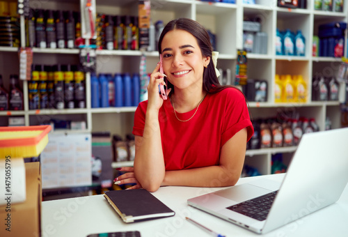 Young saleswoman smiling and talking on the phone while working at the counter of her auto parts store