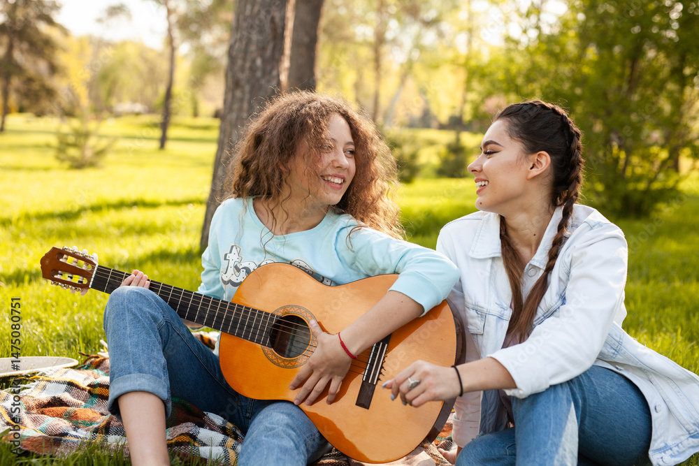 Two friends share a joyful moment sitting outdoors in a sunny park, playing the guitar and enjoying each other's company, perfectly capturing friendship, happiness, and the love of music. Two friends share a joyful moment sitting outdoors in a sunny park, playing the guitar and enjoying each other's company, perfectly capturing friendship, happiness, and the love of music.