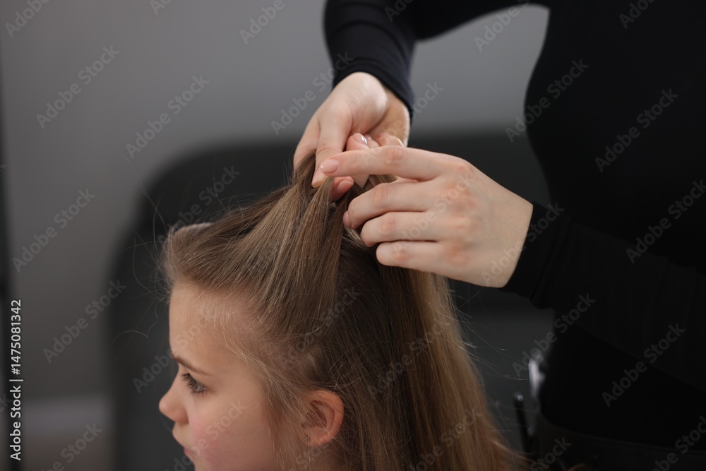 Naklejka premium Hairstylist braiding girl's hair in salon, closeup