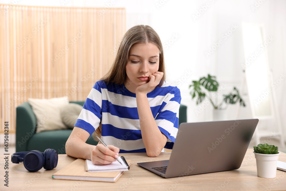 Fototapeta premium Teenage girl doing homework with laptop at wooden desk indoors