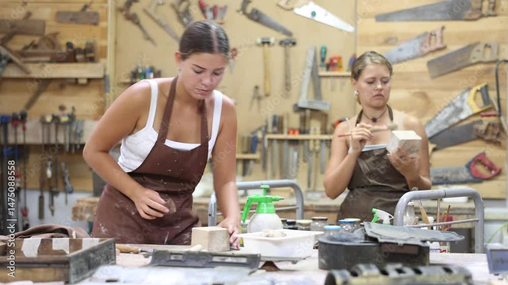 Girl is busy in carpentry workshop. Process wooden billet, sand it, applies pattern with cutter. Related stages of working with devices tools. In workshop girl stand with work gloves in hands