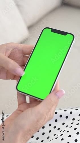 Smartphone with Green Screen in Woman's Hands, Sitting Comfortably on Sofa, Digital Interaction, Touch screen Usage, Wireless Connection, Home Setting, Chroma Key for Video Editing or Mockups