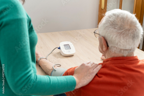 Nurse checking blood pressure of elderly man using a tensiometer, providing healthcare and monitoring vital signs