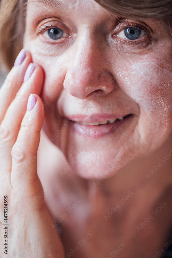 Fototapeta premium Close-up of the face of a mature woman applying a moisturizing white cream. An elderly lady takes care of her facial skin. A pensioner with a serum.