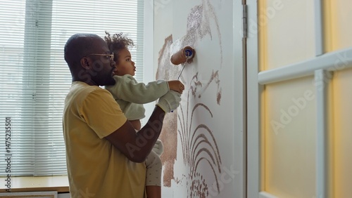 Wallpaper Mural African American father holding young daughter while together painting walls using roller in home. Child eagerly helping, spreading paint on wall creating patterns Torontodigital.ca