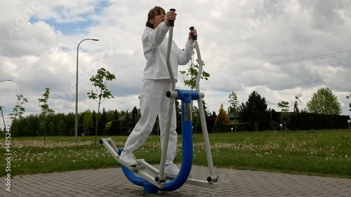 Athletic girl exercising on elliptical machine in public park, outdoor fitness activity.