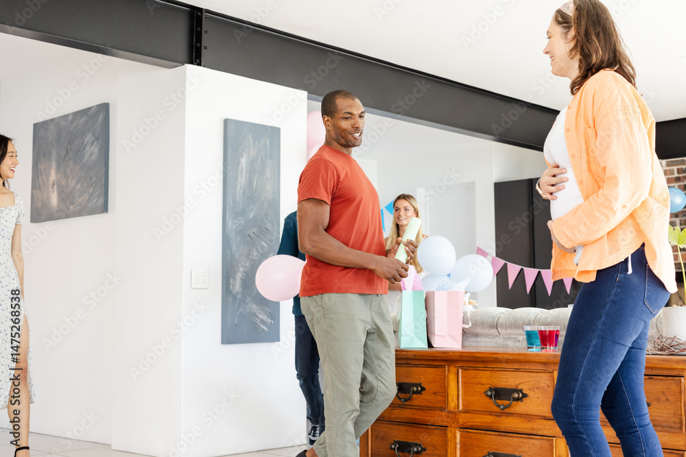Obraz premium Friends celebrating baby shower at home, smiling and holding balloons and gifts
