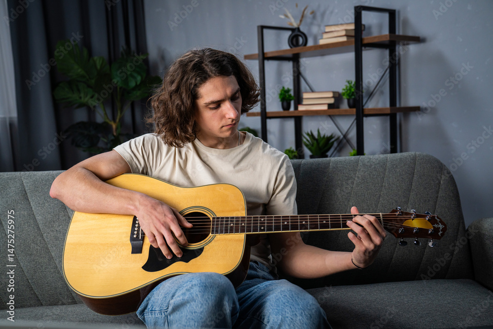 Obraz premium Young Man Practicing Acoustic Guitar at Home on a Cozy Couch