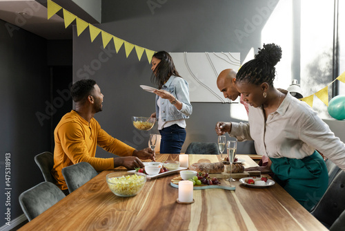 Friends enjoying dinner party, sharing food and laughter around wooden dining table