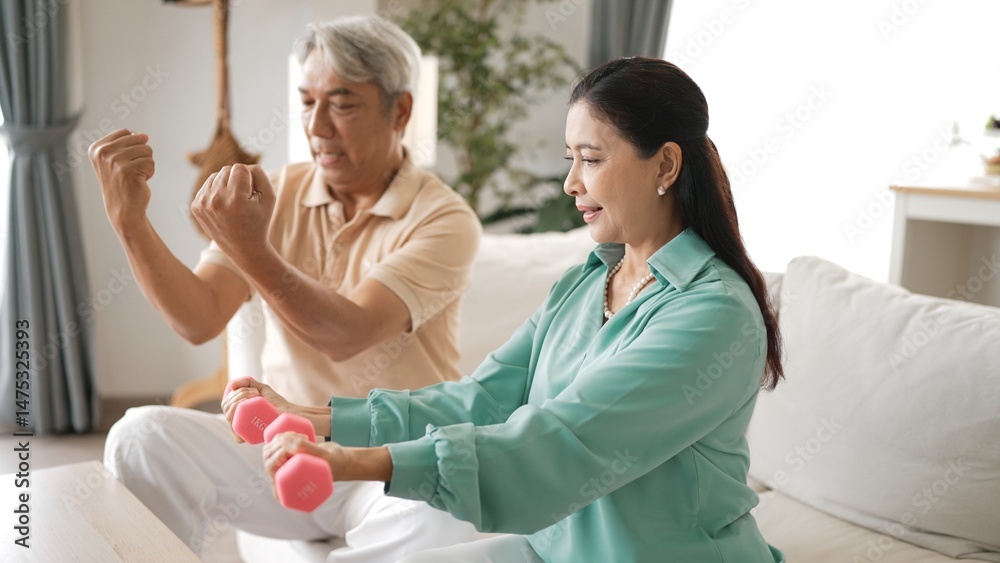 Obraz premium Happy elderly couple exercising together with dumbbells at home, focusing on muscle strength, joint health, and physical wellness for improved mobility and healthy aging. Retirement concept. Myrmidon.