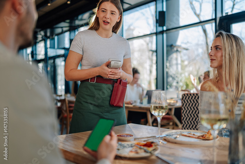 Waitress holding pos terminal accepting mobile payment from customer in restaurant