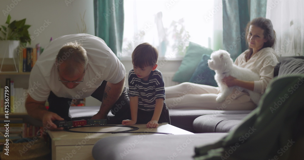 Fototapeta premium Family spending time together in cozy living room, grandfather playing with young boy, mother smiling with pet dog on couch, warm and homely atmosphere, bonding moment
