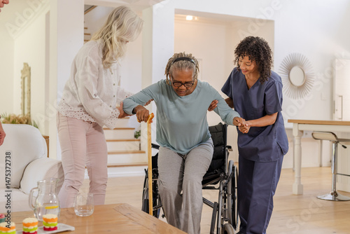 Assisting African American senior woman, caregivers helping transition from wheelchair at home