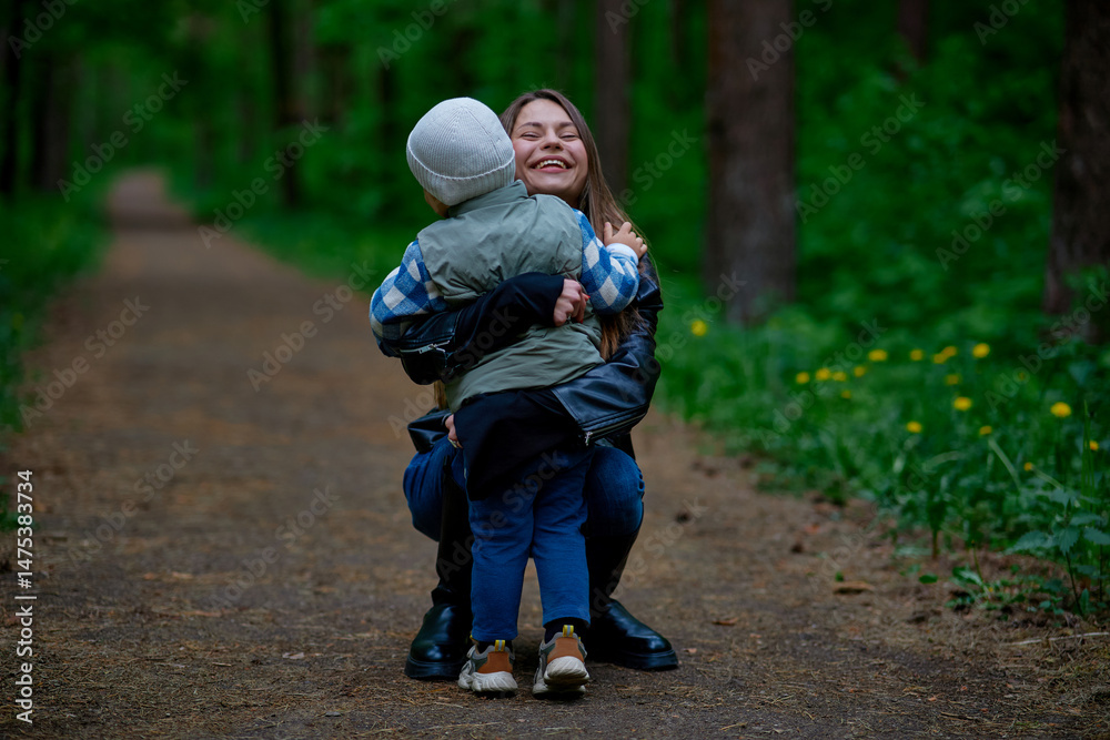 Fototapeta premium A joyful woman hugs a child on a forest path, sharing a heartfelt moment in nature. Surrounded by greenery and trees, they express love, warmth, and connection in an outdoor setting.