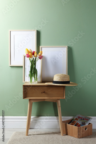 Empty picture frames, straw hat and beautiful tulips near pale green wall indoors