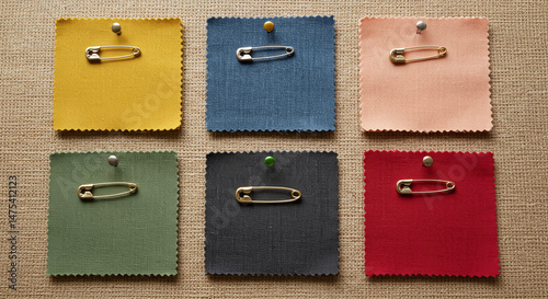 Colorful fabric swatches with safety pins on textured surface