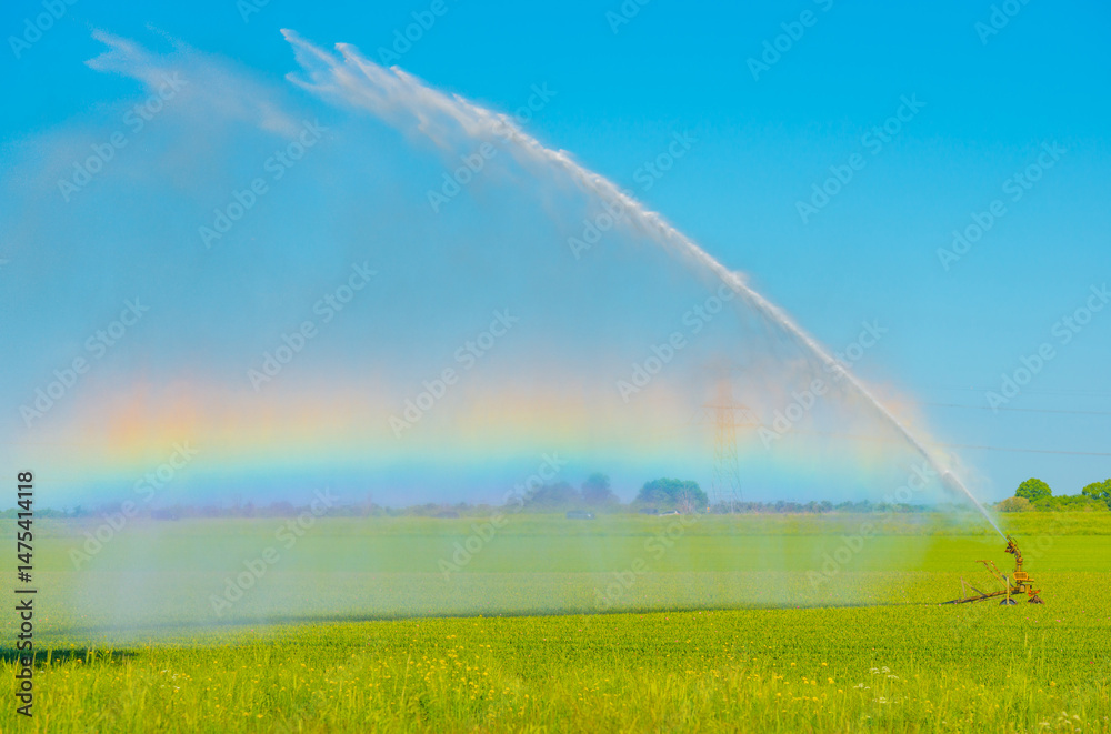 Naklejka premium Irrigation equipment in an agricultural field causing a rainbow and watering dry land in springtime, Almere, Flevoland, The Netherlands, May 12, 2025