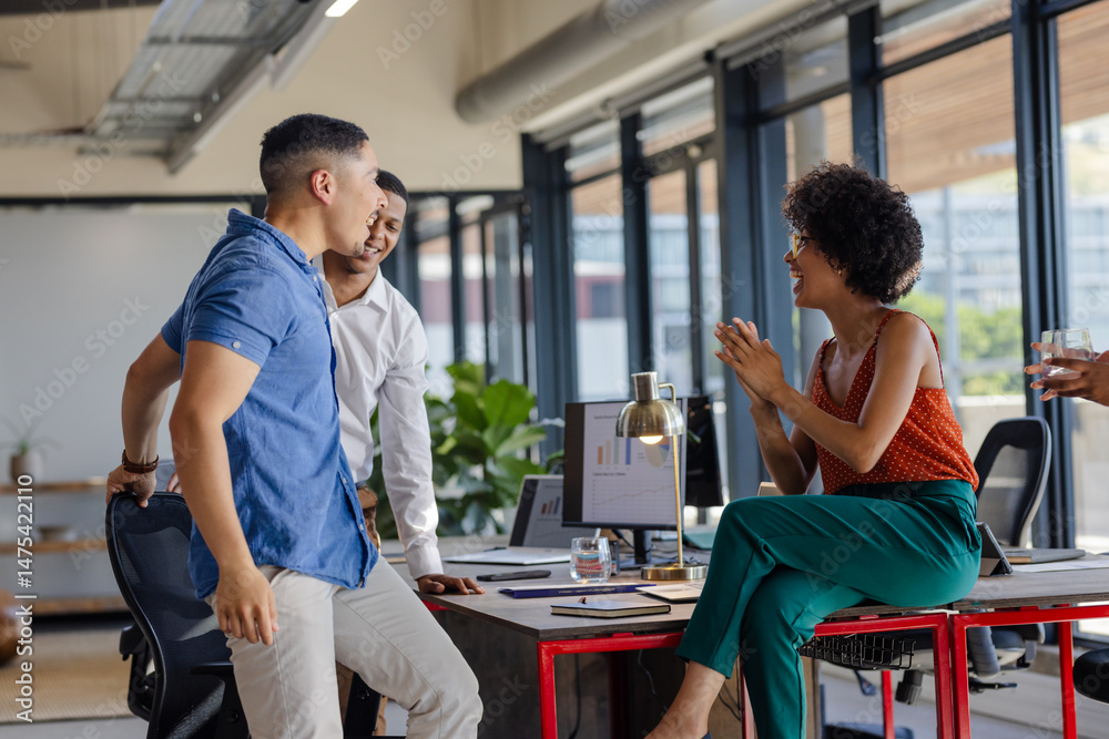 Fototapeta premium Colleagues discussing project at office desk, sharing ideas and smiling