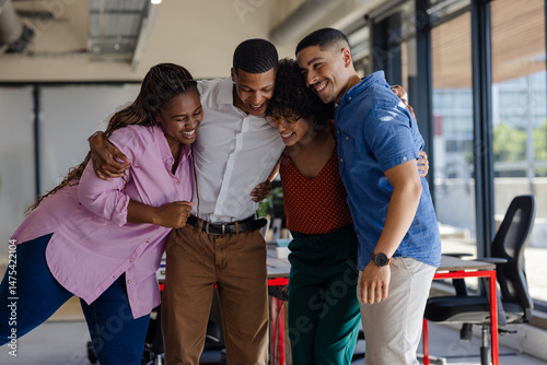 Diverse colleagues embracing and laughing together in modern office setting
